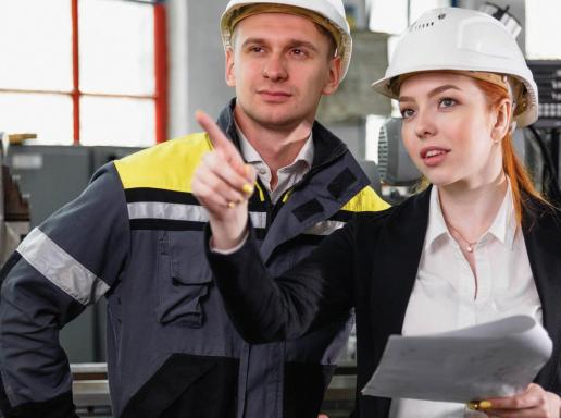 Man and woman in hardhats, woman directing man while holding digital tablet