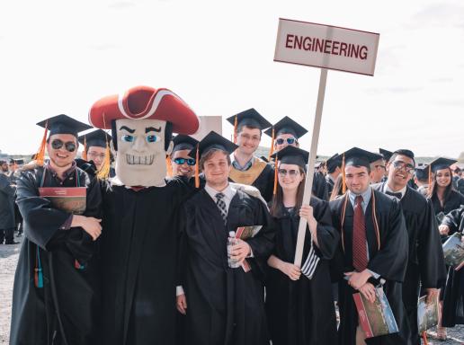 engineering grads in cap and gown with Sam the Minuteman