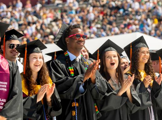 Students in cap and gown stand and clap at university commencement