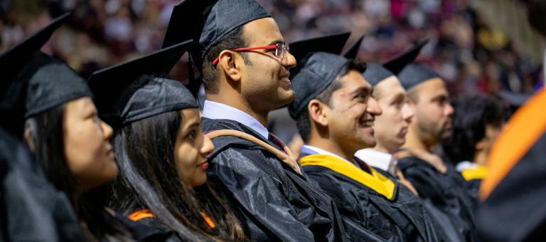 Graduates, in cap and gown, sit in a row at Commencement