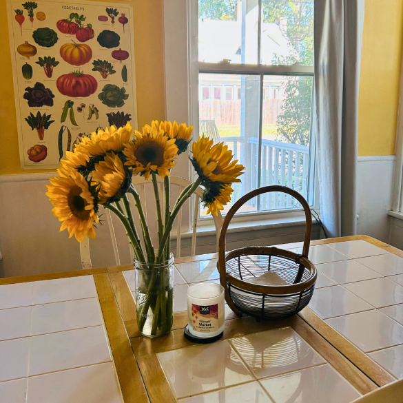 Photo of sunflowers in a vase, a candle, and a basket on a dining room table