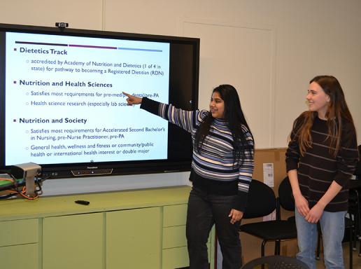 Nutrition peer advisors point to a monitor displaying the tracks available to Nutrition majors