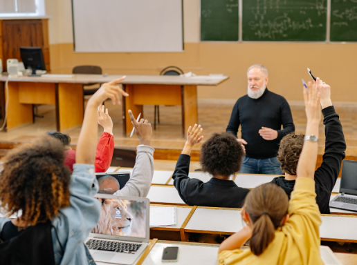 Group of students in a lecture hall. A number of students have their hands raised to ask a question.