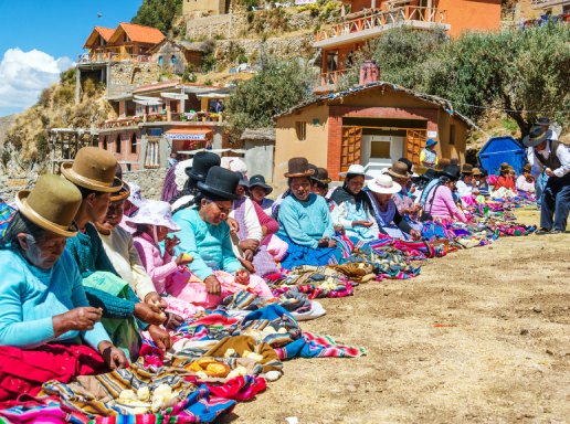 Women wearing colorful clothing and hats, sitting on the ground and working on individual projects. 